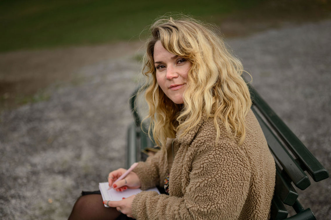 Ung kvinne sitter på en benk og noterer i en skrivebok 