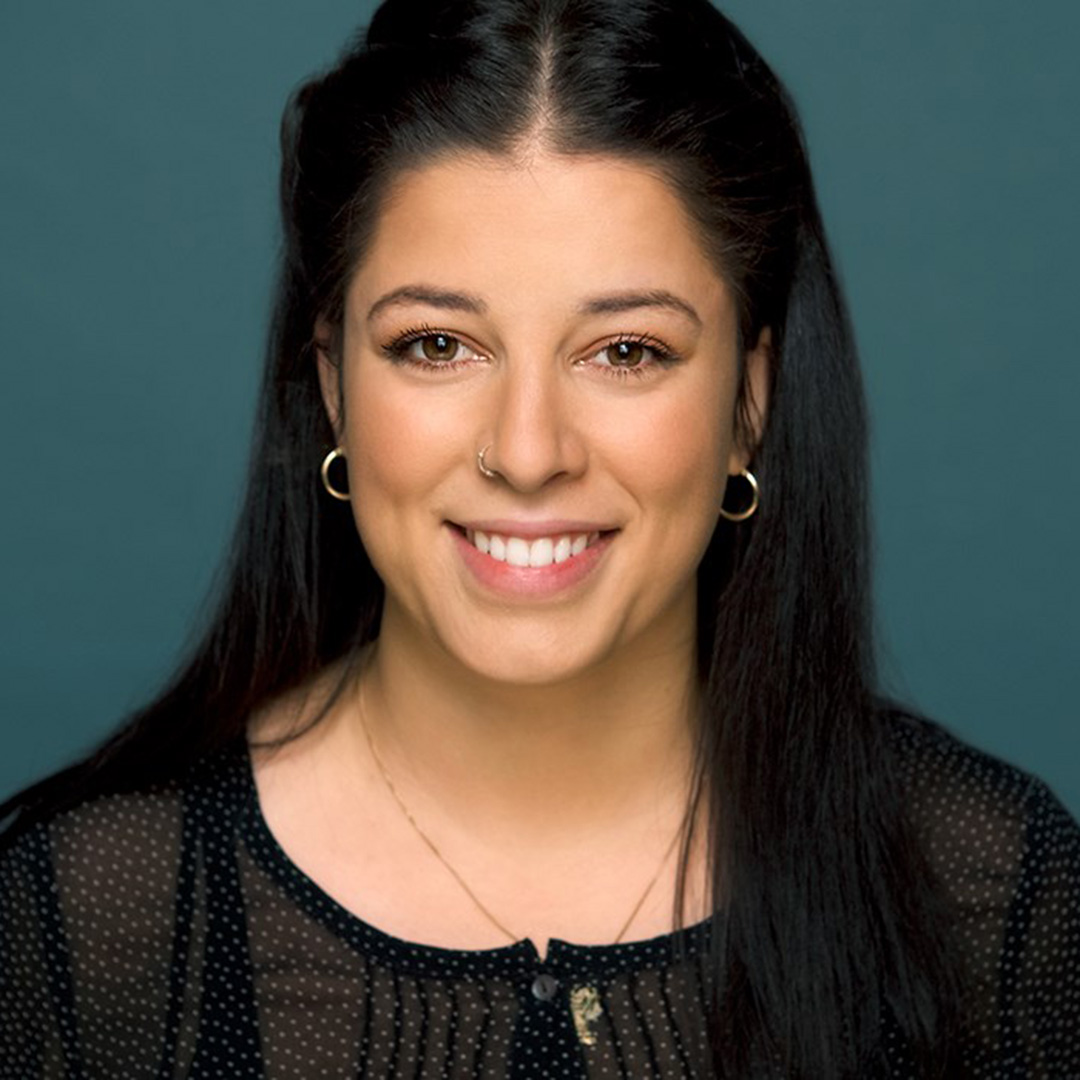 Keemy Katrin Haugland har langt, sort hår. Hun har gullringer i ørene, et gullsmykke og piercing i nesen. Hun har på seg en sort bluse med hvite prikker og smiler til kamera.