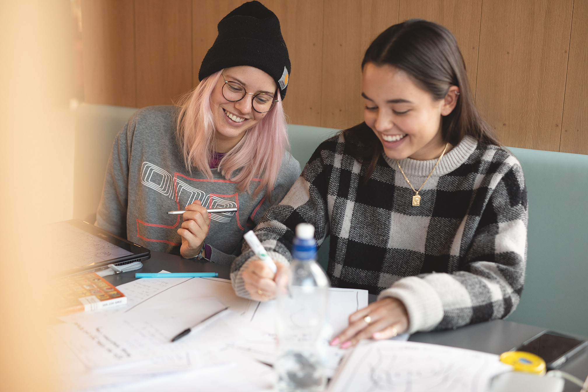 Bilde av to kvinnelige studenter som sitter i en sofa og gjør skolearbeid på et bord.
