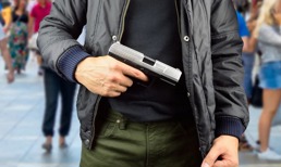En mann står med en håndpistol foran seg ute i offentligheten
