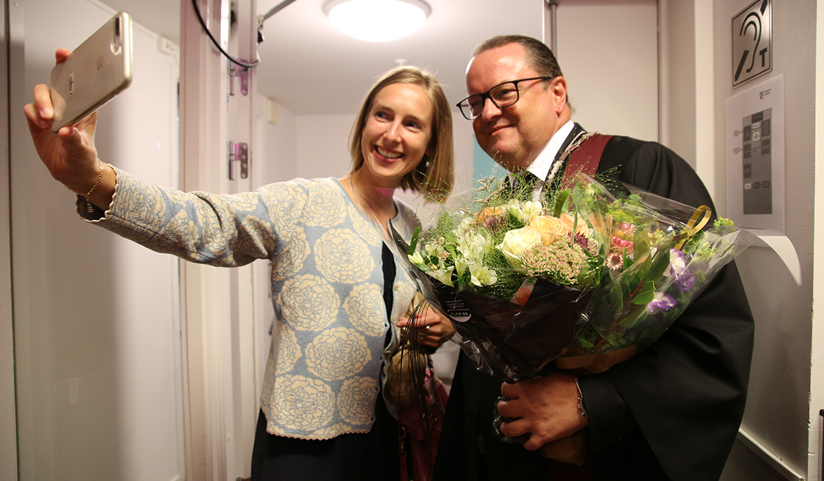 Kvinne tar selfie av seg og rektor med kappe og blomsterbukett.