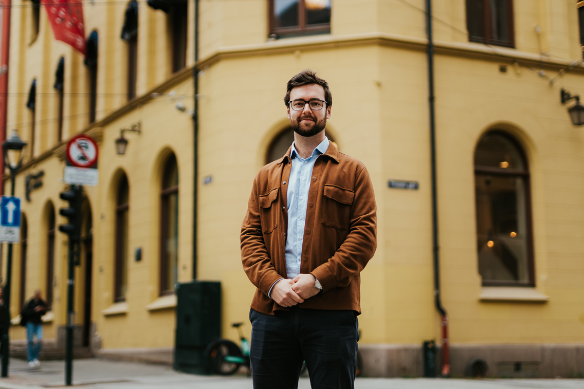 Kristiania-student Even Malmøy står utenfor ett av Kristianias bygg i kvadraturen. Han har armene foldet foran seg og smiler. Foto.
