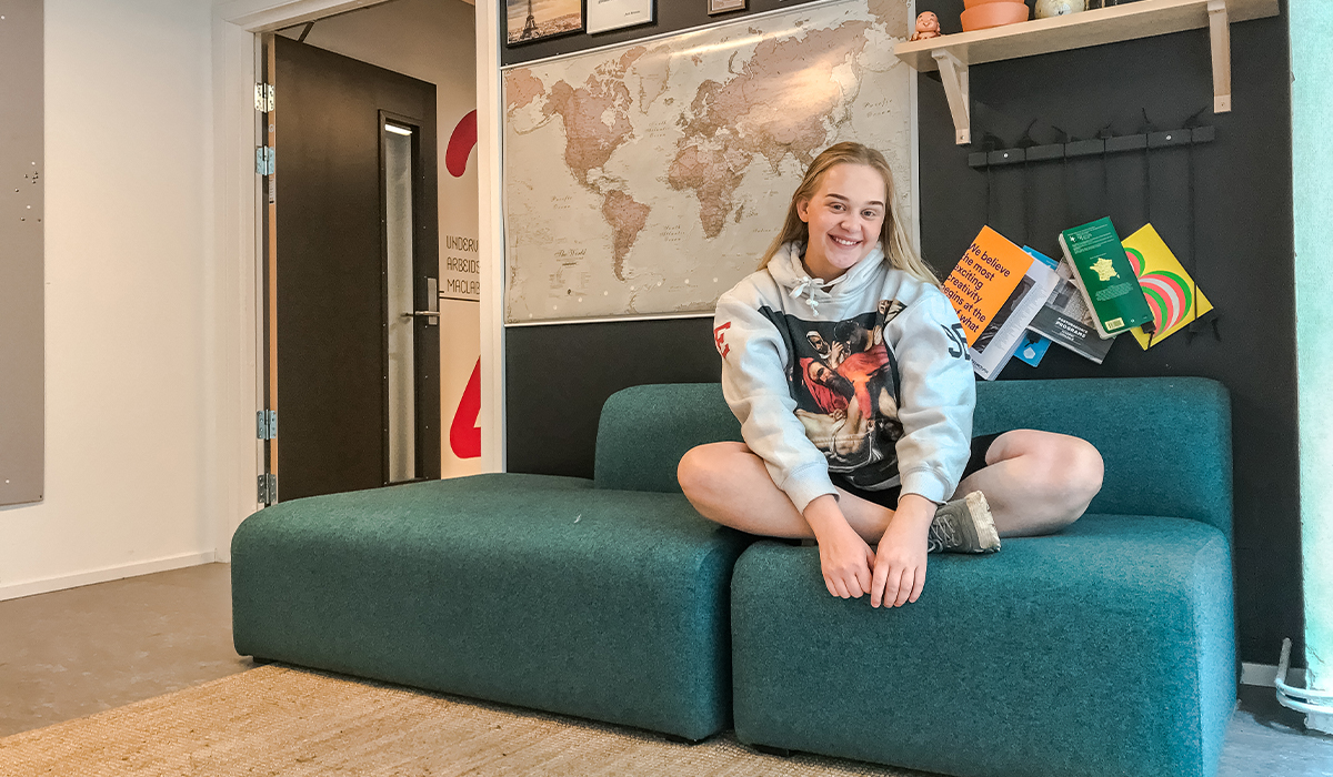 Maren sitter i en blå sofa på Campus Fjerdingen. Hun har på seg hettegenser og smiler til kamera.