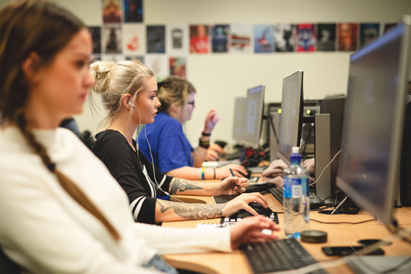 Foto av tre kvinnlige studenter som sitter i et klasserom og jobber på hver sin PC.