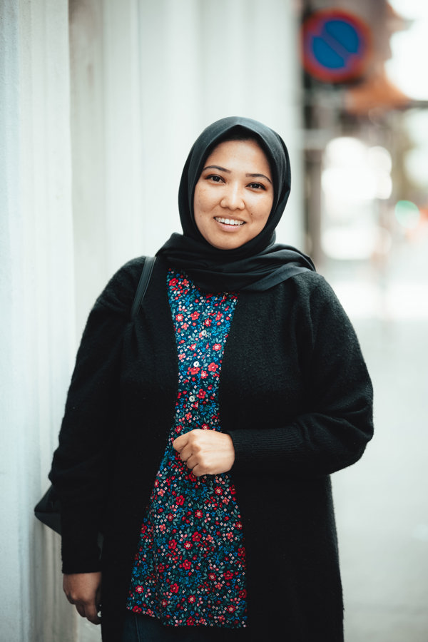 Ung kvinne i hijab står like ved en vegg på gaten og smiler til kamera.