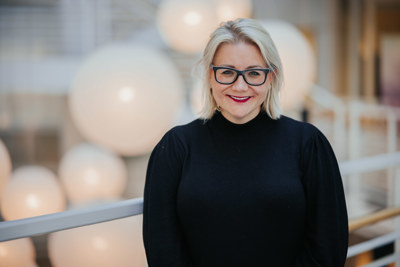 Kvinne med blondt hår og briller ikledd sort genser.