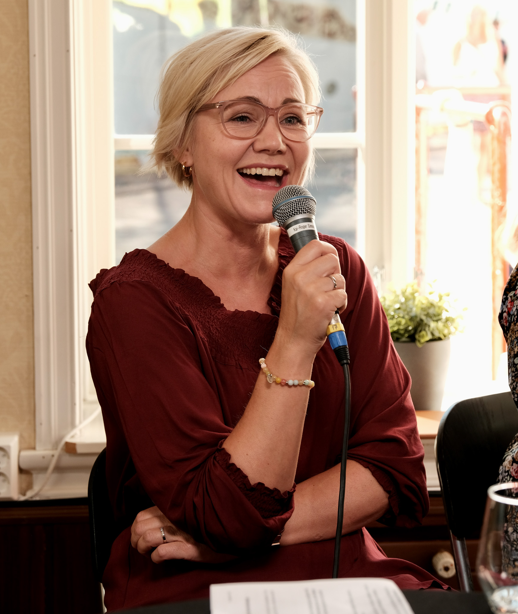 Ingvild Kjerkol fotografert under debatten. Hun sitter, har på seg en rød kjole og smiler mens hun holder en mikrofon.