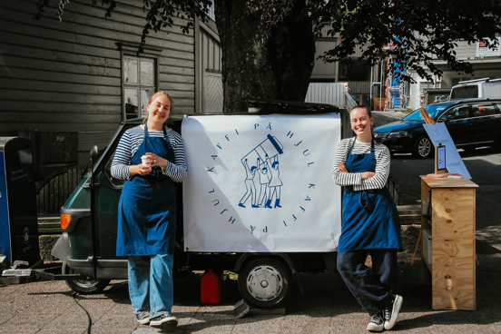 Hannah Linea Støten (24) og Andrea Bjugan (23) står foran kaffebilen sin med en stor plakat med logoen til studentbedriften Kaffi på hjul.