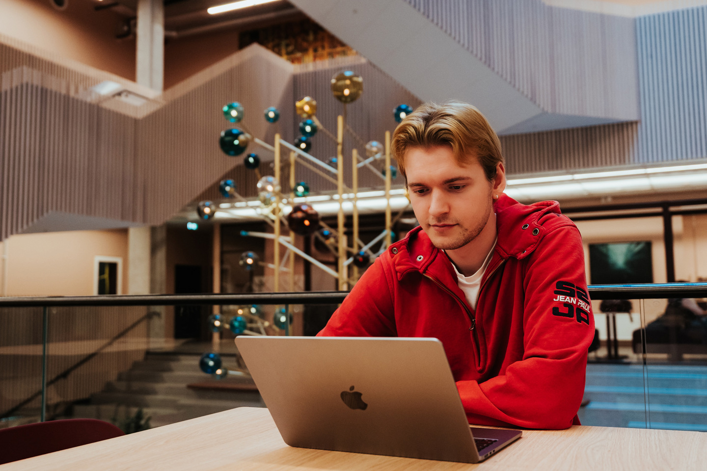 Student sitter i fellesområde foran trapp og jobber på mac.