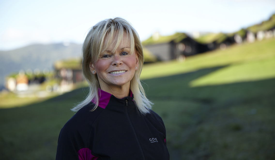 Elin Bolann står på en seter med blå himmel og grønne glessplener rundt. Hun har på seg en treningsjakke og ser rett inn i kamera og smiler. Håret hennes er blondt og øynene blå.