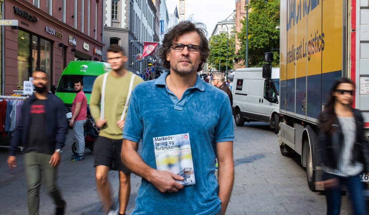 Karl-Fredrik Tangen står utendørs og holder frem sin nye fagbok «Markedsføring og forbrukerne» mens han ser på kamera