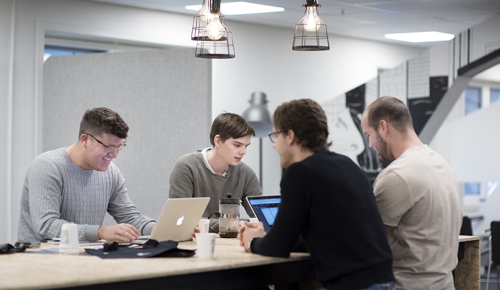 Foto av mannlige studenter som sitter rundt et bord med hver sin laptop.
