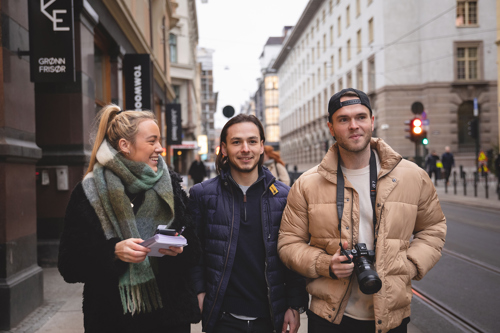 Bilde av en kvinnelig og to mannlige studenter med notatblokker og kamera i henda.