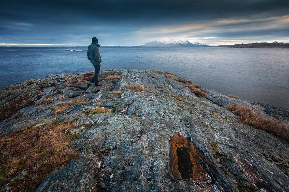 Mann ser utover havet mot fjell i horisonten