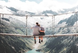 Et par sitter på en hengebru over en fjord med vakker utsikt