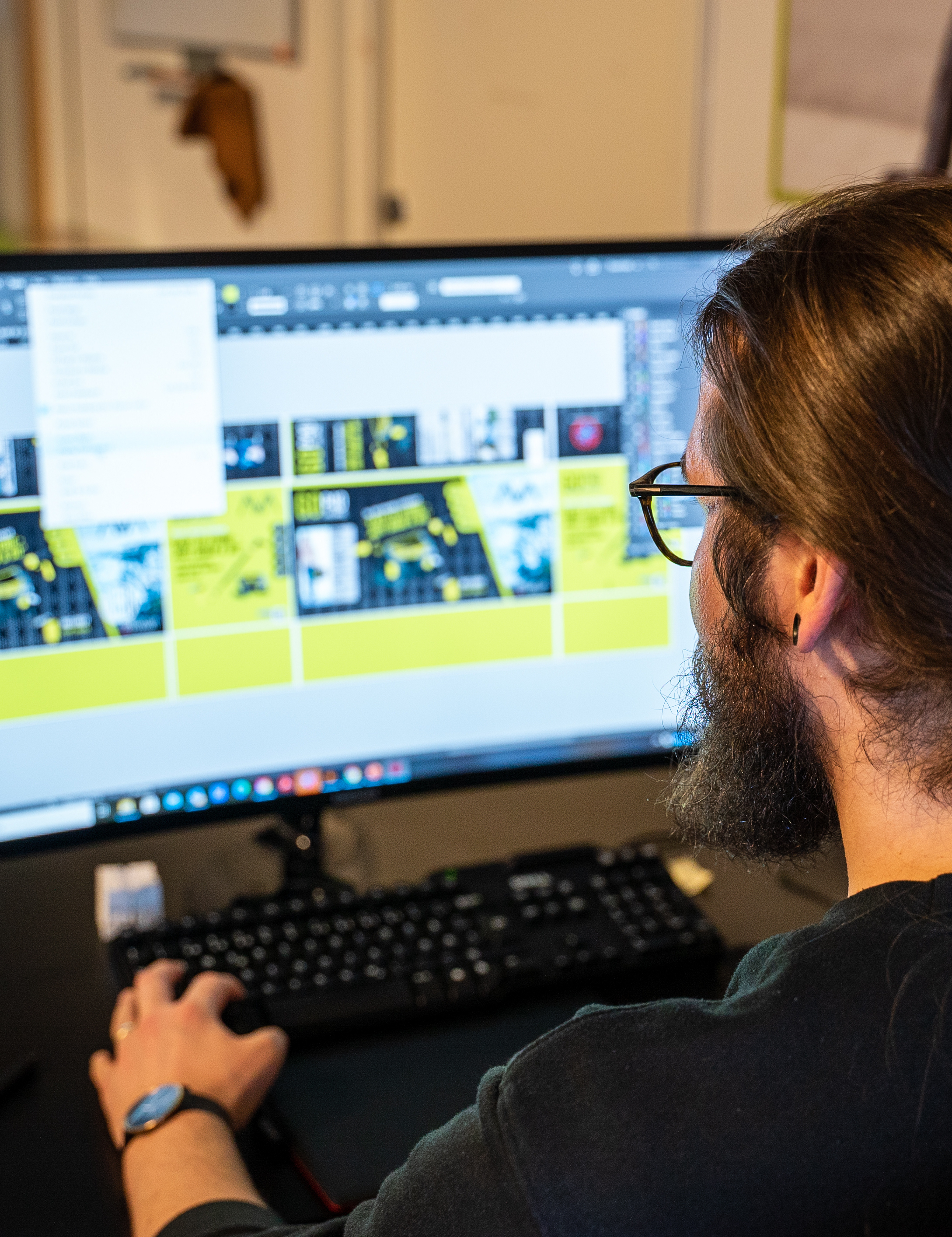 Christopher sitter foran en pc skjerm. På skjermen jobbes det med grafisk design.