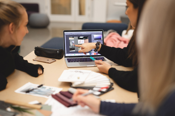 Studenter diskuterer interiørdetaljer rundt en Mac. Bachelor i interiørarkitektur ved Høyskolen Kristiania.