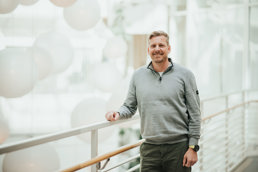 Mann i grå genser smiler til kamera.