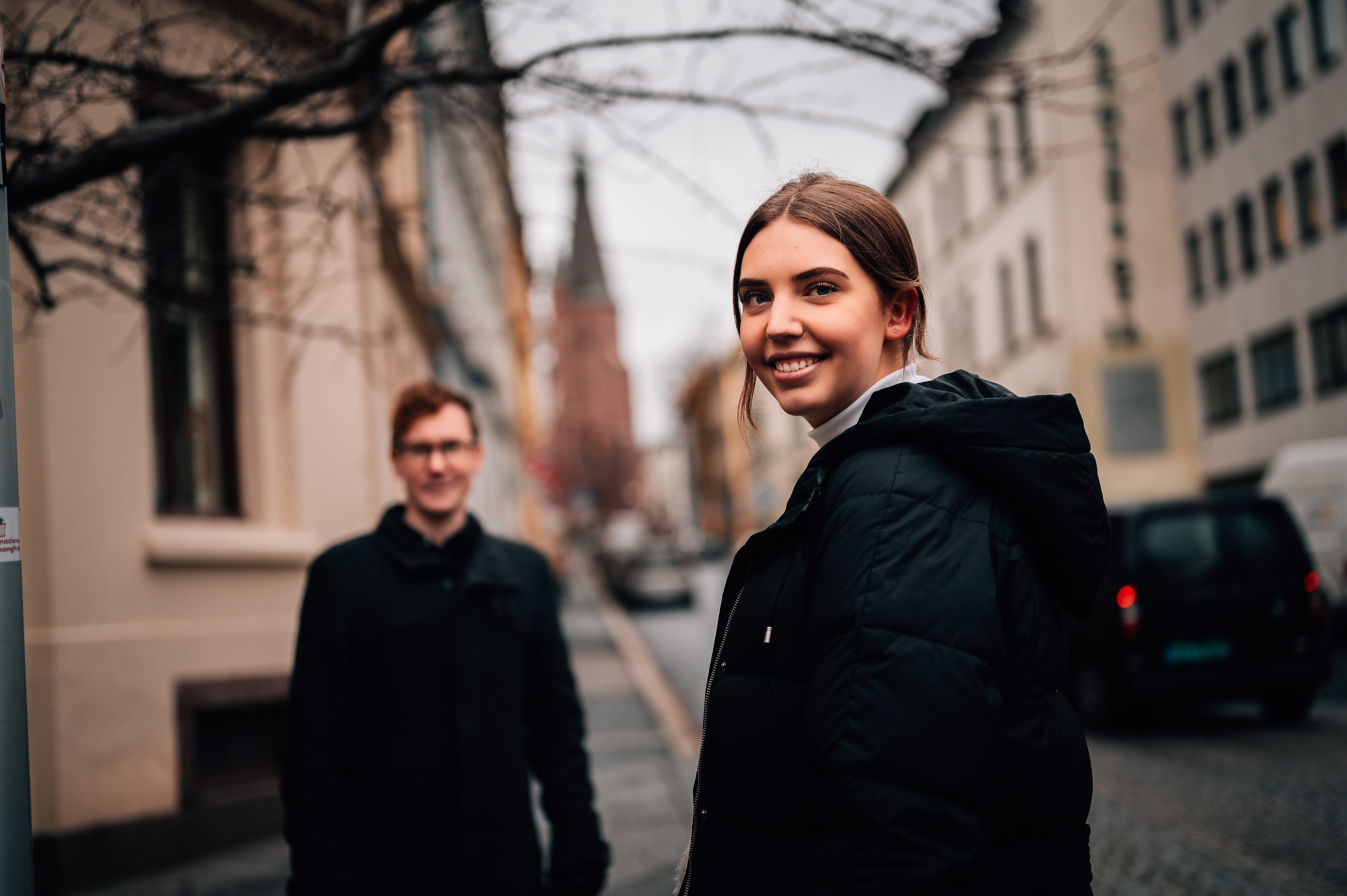 Two students standing in a street in Oslo, with a couch behind them