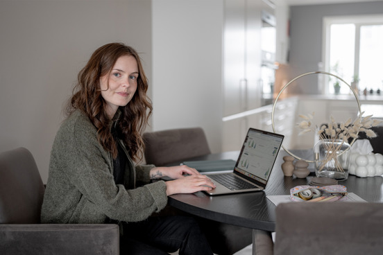 Kvinne ved pc smiler i kamera