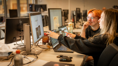 To studenter samarbeider ved foran en PC med spillgrafikk.