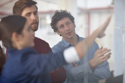 Three co-workers discussing something on a whiteboard in a conference room