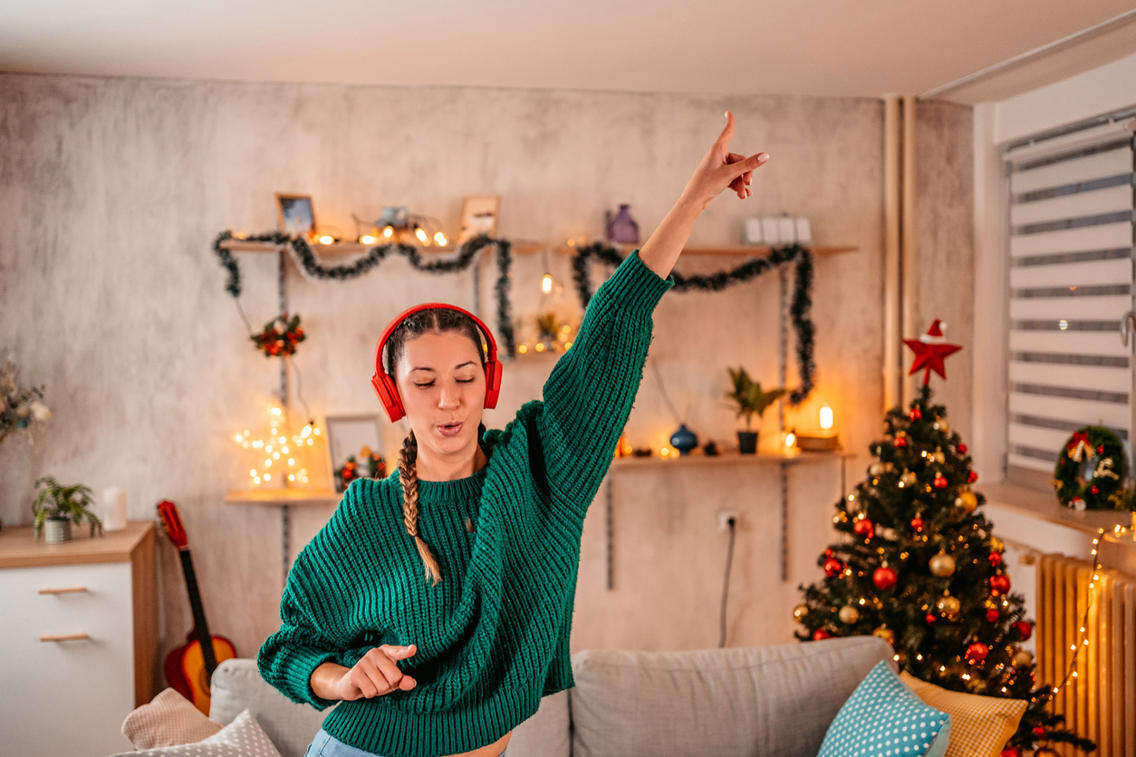 Kvinne i grønn genser danser med headset i stue med juletre