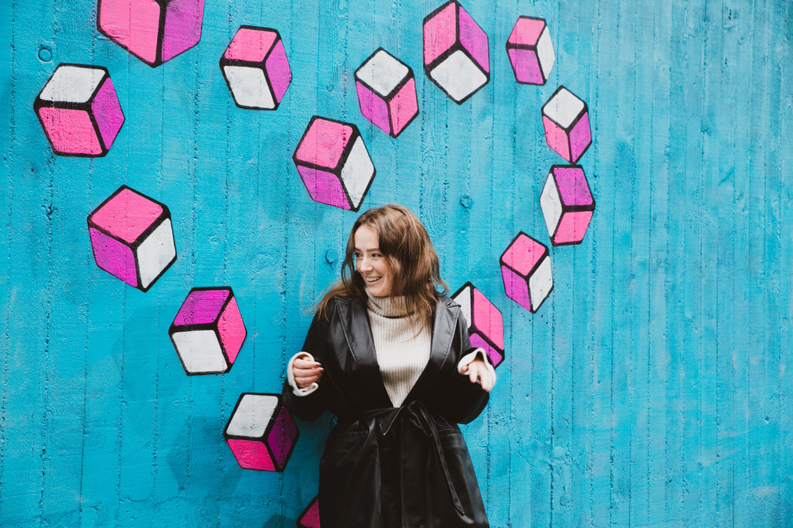 Maren står foran en grafittivegg med et rosa hjerte i bakgrunnen.  