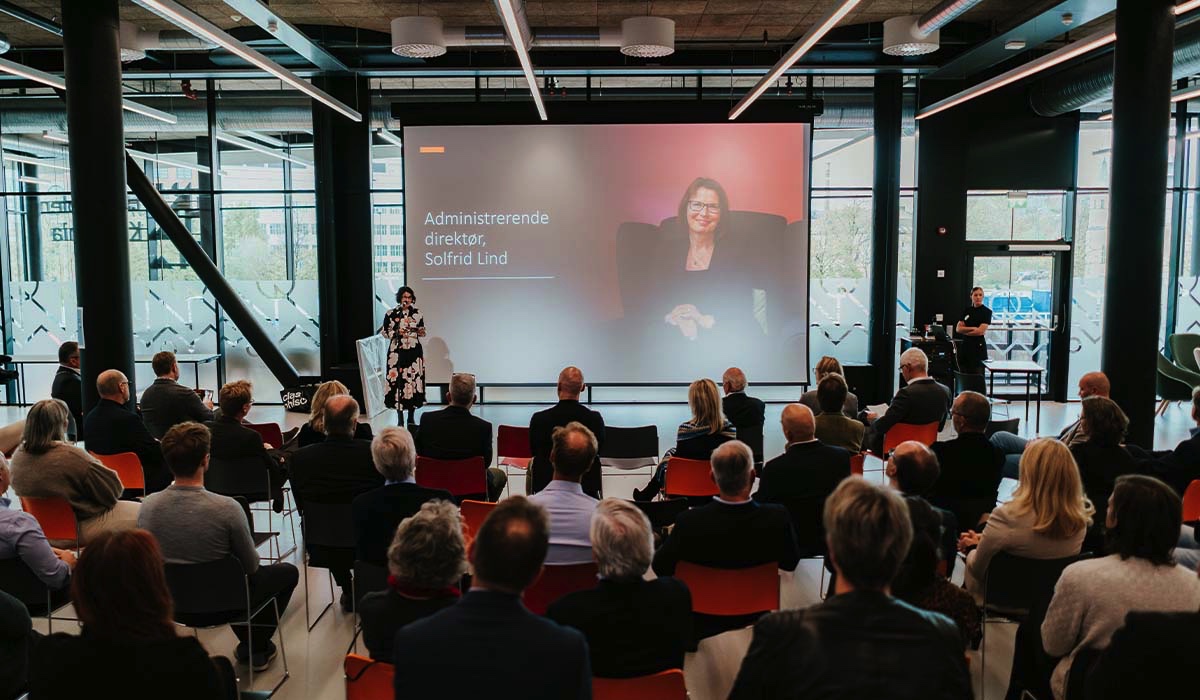 Gjester sitter samlet og lytter til administrerende direktør Solfrid Lind som taler i mikrofon til forsamlingen under åpningsseremonien.