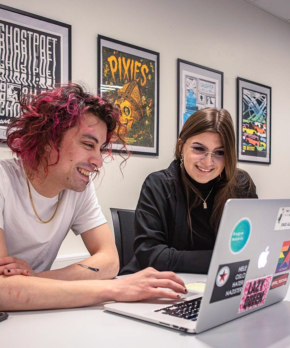 Foto av mannlig og kvinnelig student som ser på en laptop-skjerm sammen.