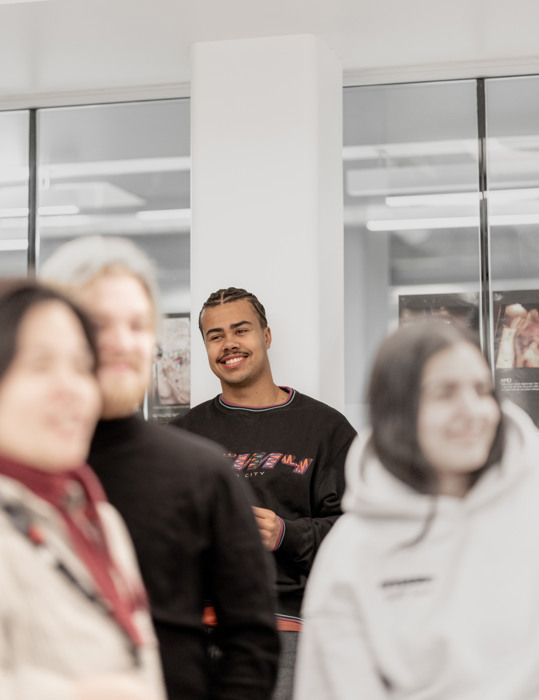 Student i fokus i et undervisningsmiljø, med andre personer uskarpt i forgrunnen.