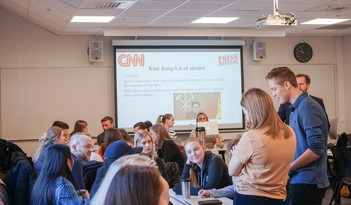 I klasserommet sitter mange studenter rundt forskjellige bord og diskuterer. På Smart Tavlen står det en fiktiv nyhetsoppdatering: «Kim Jung-Un er savnet».