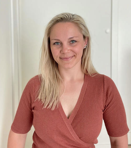 Bilde av blond kvinne i lyserød topp som smiler til kamera.
