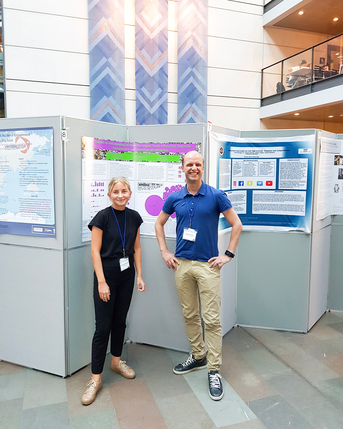 Mathilde og Kjeld Hansen på konferansen i København. De står foran posteren til Mathilde. Mathilde har på seg en mørkeblå jumpsuit og har håret bak i en hestehale og Kjeld står med armene i hoftene.