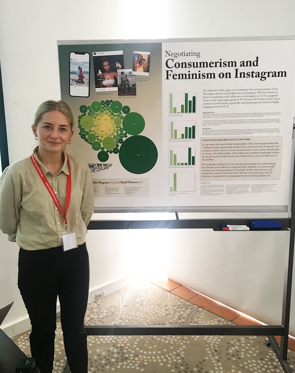 Mathilde står foran posteren sin på konferansen i Melbourne. Hun har et nøkkelbånd med rød tråd. Hun har på seg sorte jeans og en bluse i beige på seg.