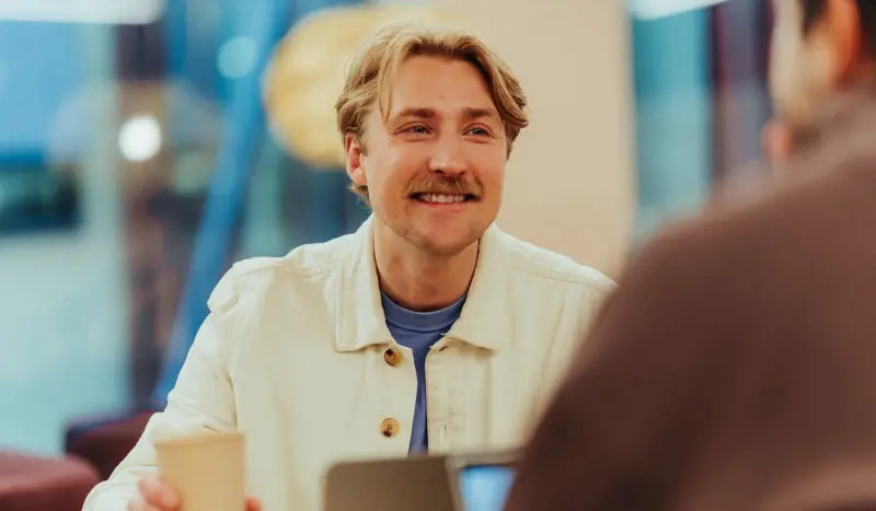Nettstudent med hvit skjorte tar en kaffe og jobber med pensum