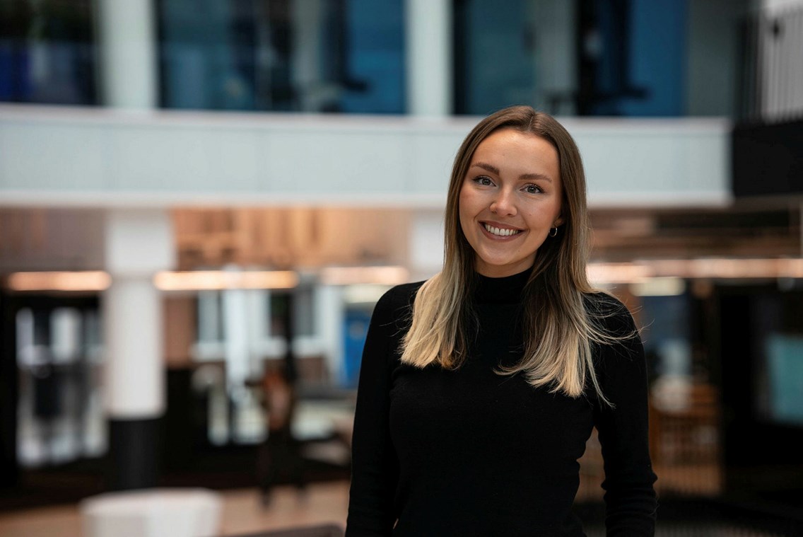 Foto av kvinne foran uskarp bakgrunn som smiler til kamera