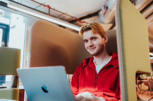 Student sitter i behagelig stor med skjerming for bedre konsentrasjon og jobber på PC.