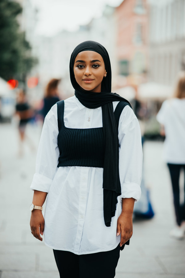 Ung kvinne i hvit skjorte og hijab ser inn i kamera