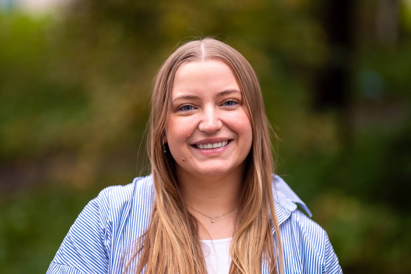 Sandra Eide står foran grøntområde i blå skjorte og smiler.