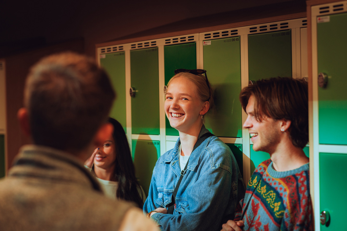Fire studenter fotografert i en gang, foran låsbare skap.