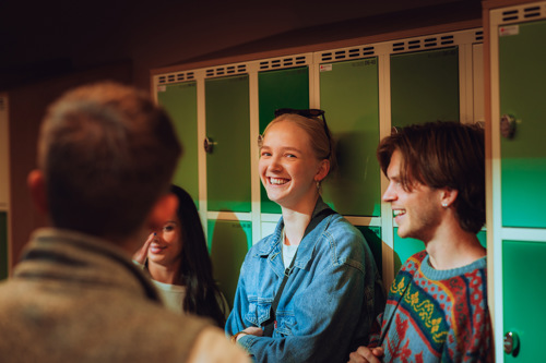 Fire studenter fotografert i en gang, foran låsbare skap.