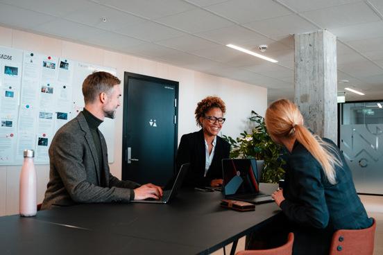 Mennesker sitter rundt møtebord og snakker.