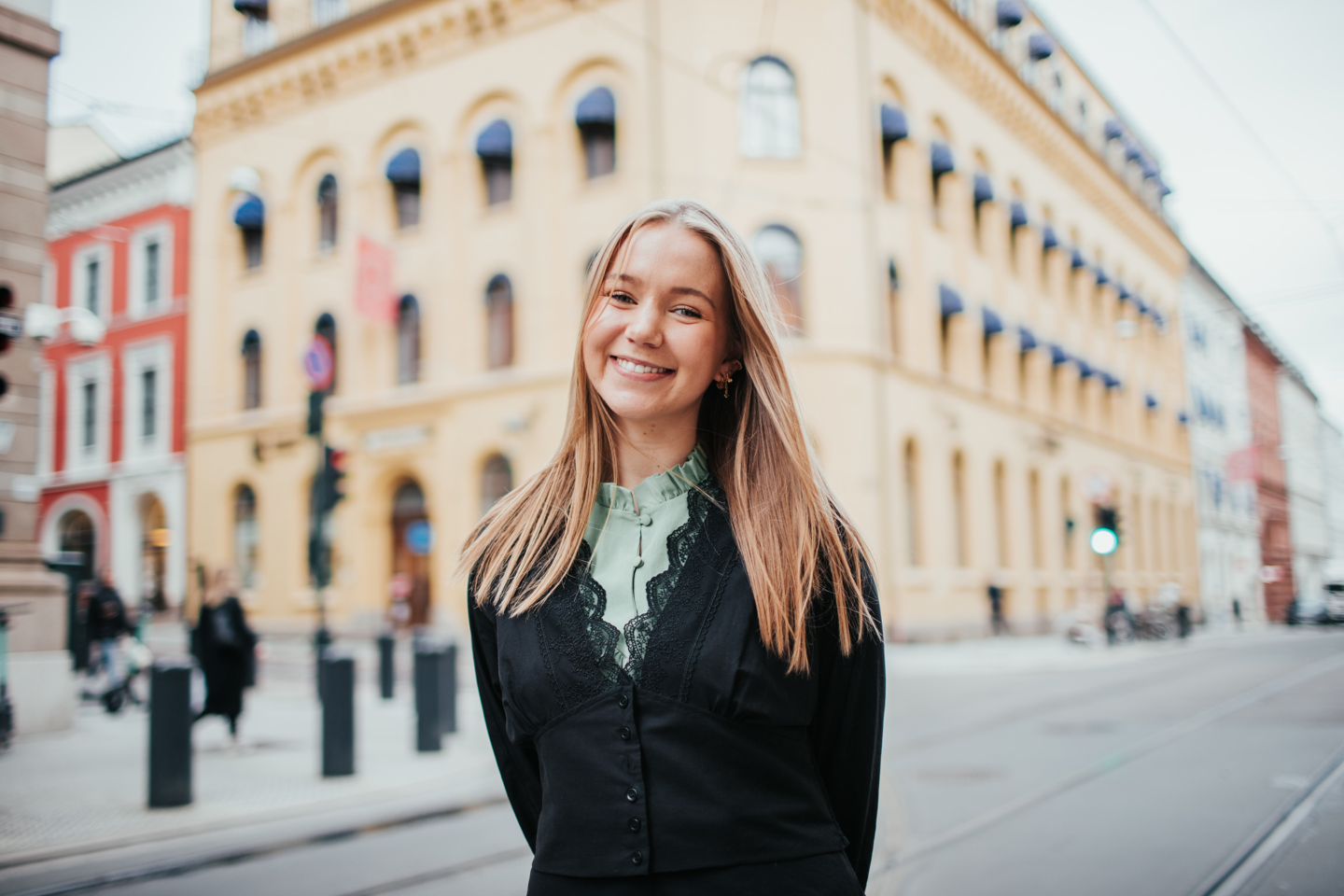 Kvinnelig student Synne Schou foran Høyskolen Kristiania sitt gule bygg i kvadraturen. Jente med mørkblondt hår, grønn topp og sort overdel.