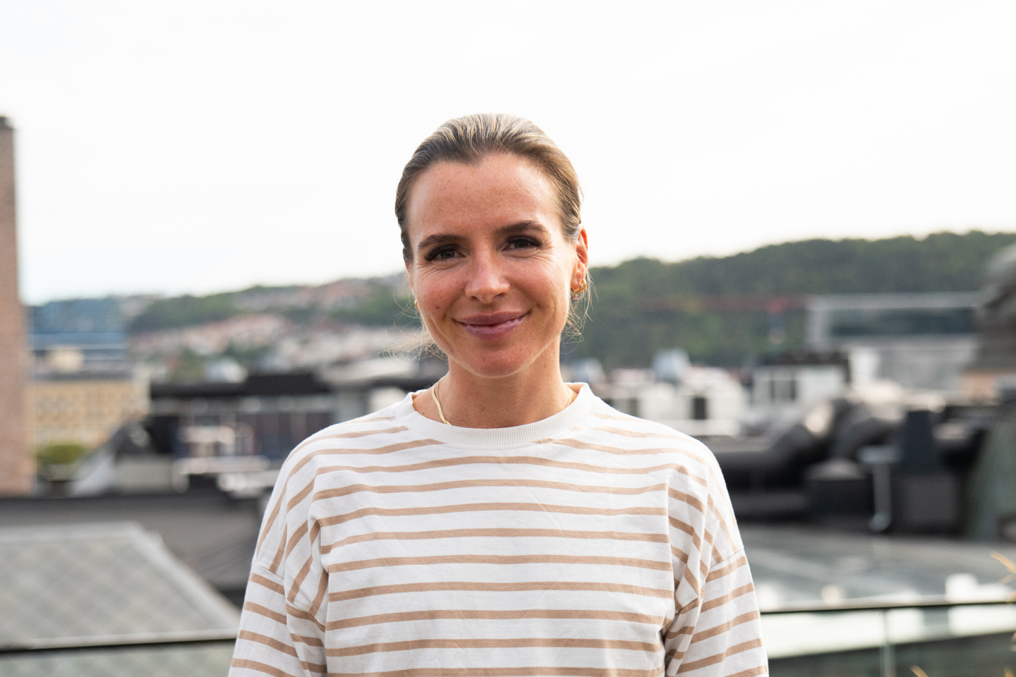 Christine smiler til kamera på en takterrasse med utsikt. 