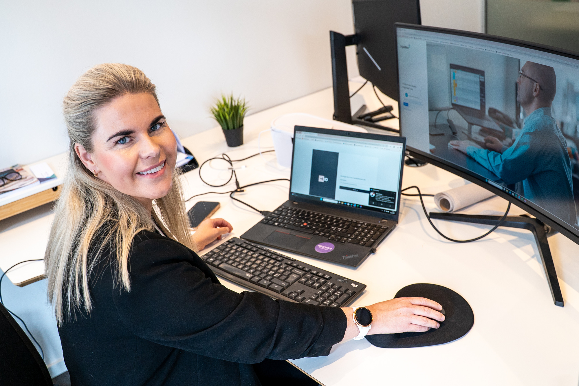Ragnhild sitter ved pulten og smiler mens hun jobber på datamaskinen sin.