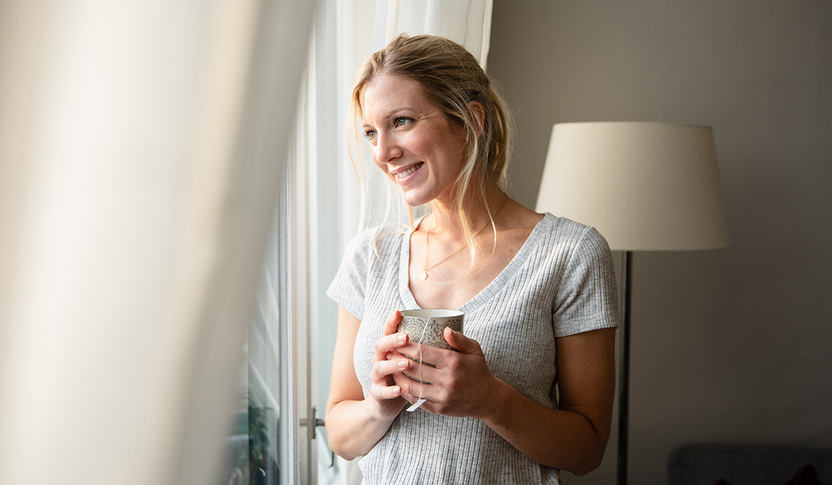 Kvinne står med kaffekoppen og ser ut vinduet