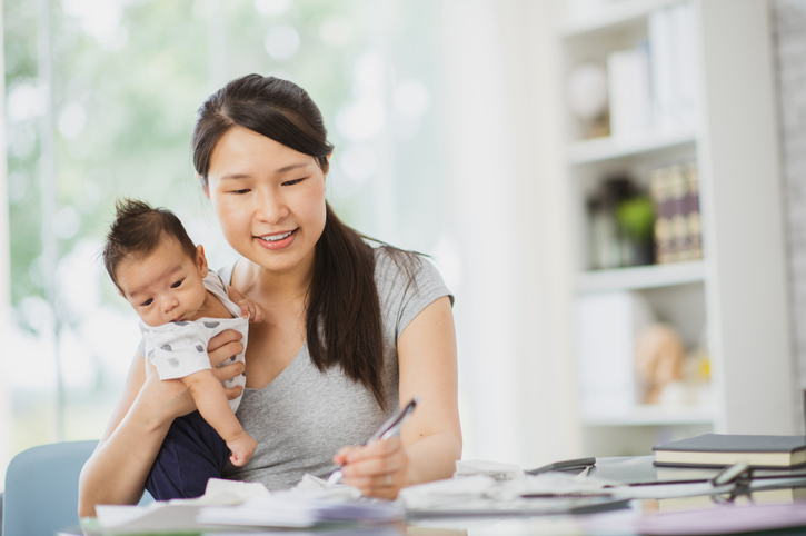Woman holding baby and writing at a desk