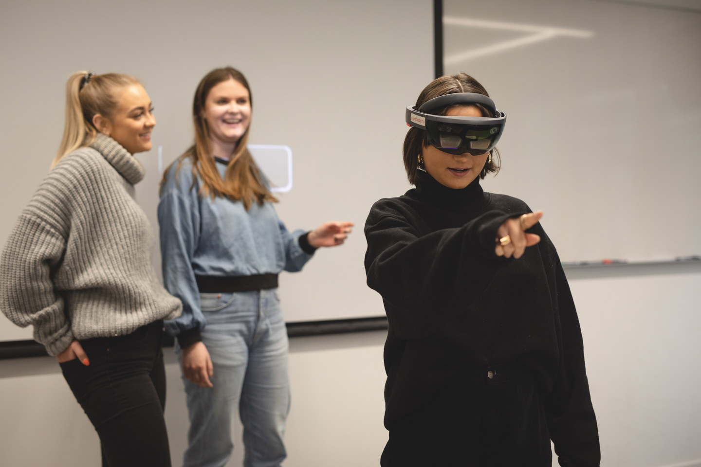 En jente i front bruker VR-briller, to venninner smiler og følger med i bakgrunnen