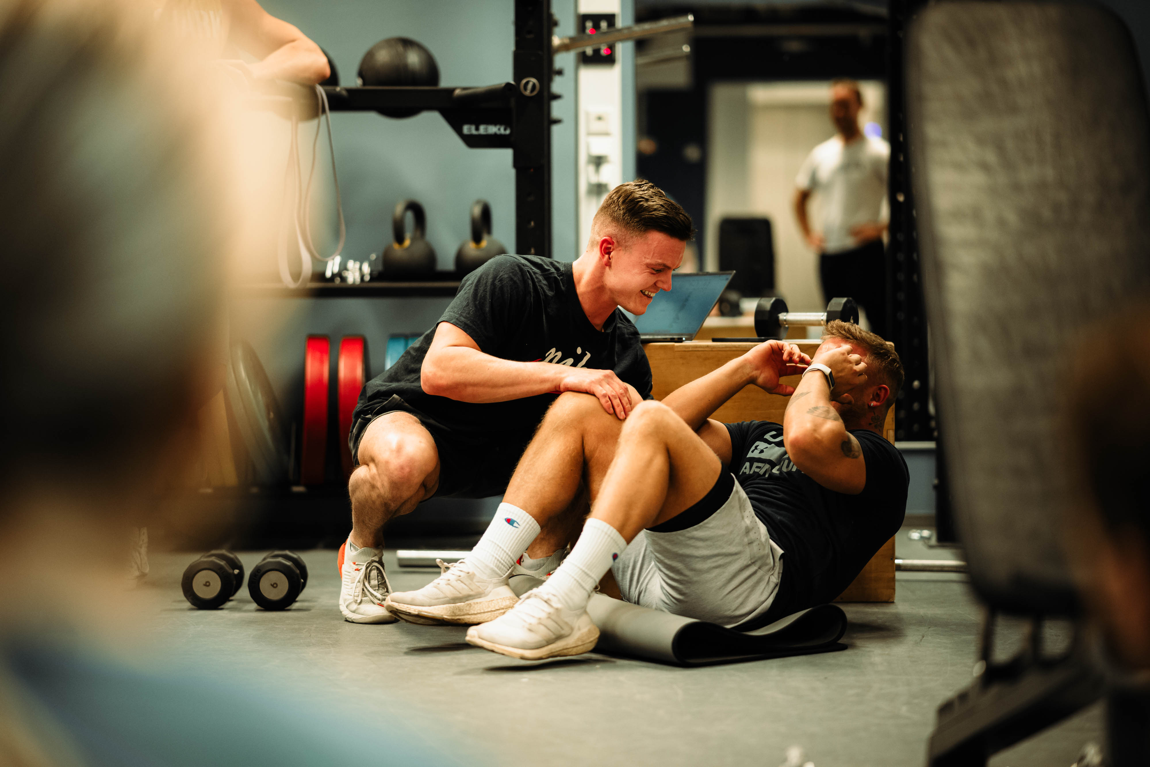 Foto av to unge menn i treningssituasjon. Den ene spotter, en annen tar sit-ups.
